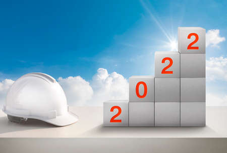 Happy New Year 2022 Construction and Industry.White Helmet and a numbered concrete cube on the desk of an engineer or construction worker.の写真素材