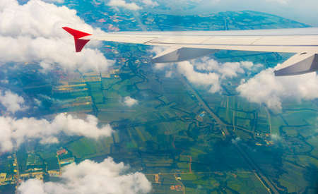 View from airplane on the aircraft white wing flying over cloud and farmland in the morning. Air travel and transportation concept.の写真素材