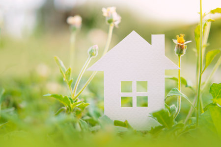 white paper house and flower in morning garden.homeless housing and home protection insurance concept, international day of families, foster home care, family, and real estate.