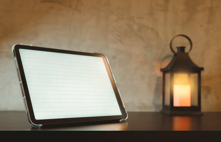 A tablet with a lined paper screen. A writer's desk at night is lit by an antique lamp.の写真素材