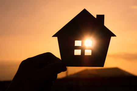 Hands holding paper house on sunset sky, family home, homeless housing, and home protection insurance concept, international day of families, new life, foster home care, and real eの写真素材