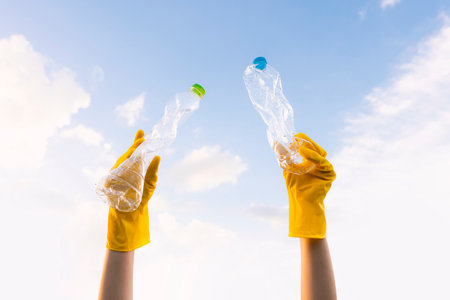 A young volunteer's hand lifts trashed plastic bottles into the sky. On World Environment Dayの写真素材