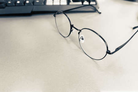 close up glasses on wooden desk with keyboard of computer