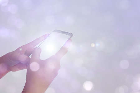 play smartphone in hand with white sunlight on bokeh backgroundの写真素材