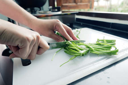 hand of woman is cutting morning glory on a cutting board With knife in the kitchen.