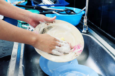 Woman's hand washing dishes fork and spoon with sink.の写真素材