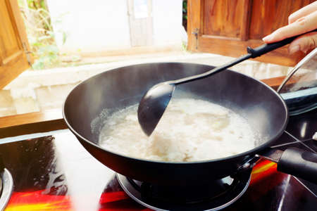 The hand of a woman is cooking with a pan And use a ladle to stir and scoopの写真素材