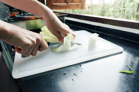hand of woman is cutting Nappa cabbage on a cutting board With knife in the kitchen.の写真素材