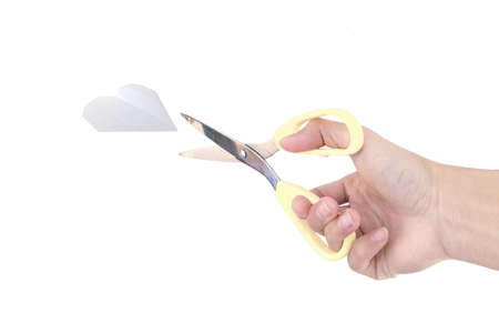 Hand holding a scissors to cut the paper heart isolated on white background.の写真素材