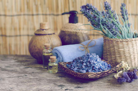 Purple scrub spa salt on wooden bowl with aroma gel, towel, body washing gel, and lavender flower, on dark purple vintage tone for health care and beauty conceptの写真素材