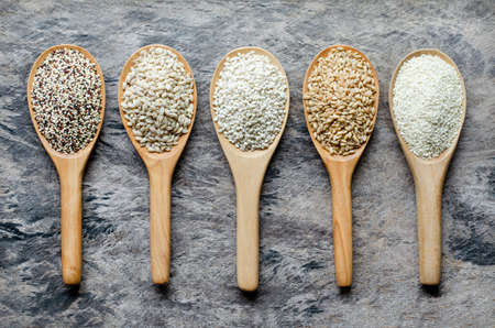 White and brown dry organic cereal and grain seeds in wooden spoon consisted of quinoa, wheat, pearl...