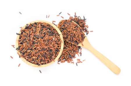 Top view of dry organic brown and riceberry rice seeds in wooden bowl and spoon on white background,...