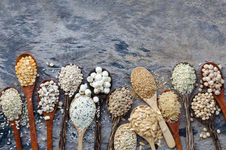Variety kinds of natural cerean and grain seeds in wooden spoon on grunge background, consisted of rice, mung, sesame, black eye pea, lotus, flax seedsの写真素材