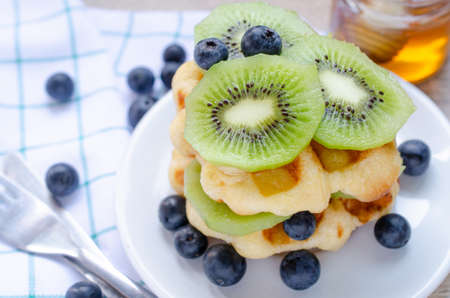 Closed up fresh sliced kiwi and blueberry fruit on top of delicious homemade waffle in white dish...