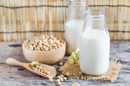 Closed up delicious homemade soybean milk in glass bottle over blur seeds in wooden bowl and spoon, for clean food homemade product or agricultural goods conceptの写真素材