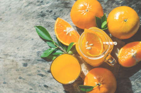 Closed up fresh sliced orange fruit on top of fresh orange juice in glass mug with some fruit on wooden table background under morning sun light in soft light toneの写真素材