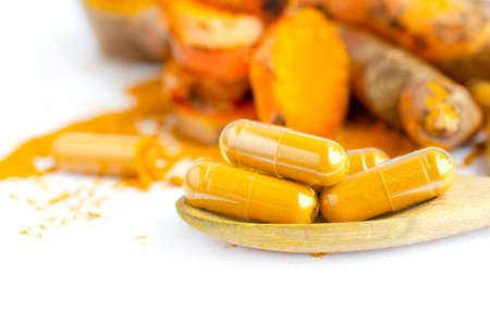 Closed up dry organic turmeric powder in capsule on wooden spoon on white backgroundの写真素材