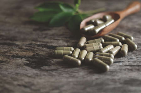 Thai herb dry powder in capsule pile on wooden spoon and grunge background in dark toneの写真素材