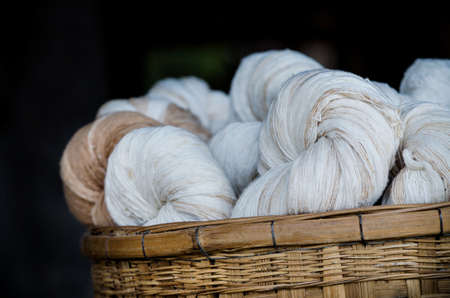 Group of handmade cotton thread bundle in wooden basket over dark background, ready for fabric or cloth productionの写真素材