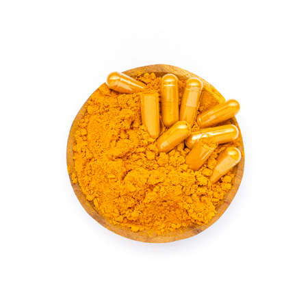 Dry organic turmeric powder in capsule and wooden spoon on white backgroundの写真素材
