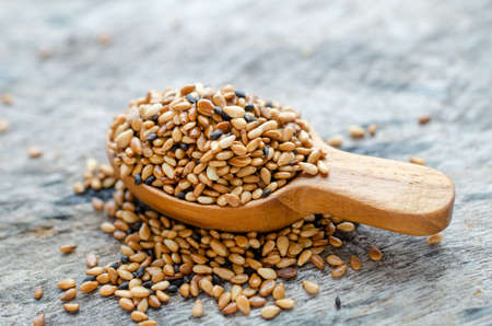 Dry organic roasted white and black sesame seed pile in wooden spoon on grunge background, for food...