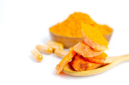 Closed up sliced organic turmeric root in wooden spoon over blur turmeric powder capsule and some in wooden bowl on white background. For natural medical product as an alternative treatment conceptの写真素材