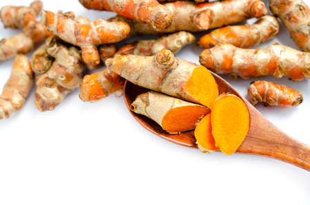 Closed up sliced organic turmeric root in wooden spoon with some fresh turmeric root on white...