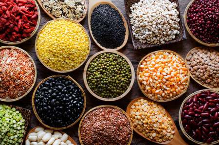 Collection of dry organic colorful cereal and grain seeds in wooden bowl in dark tone, consisted of...