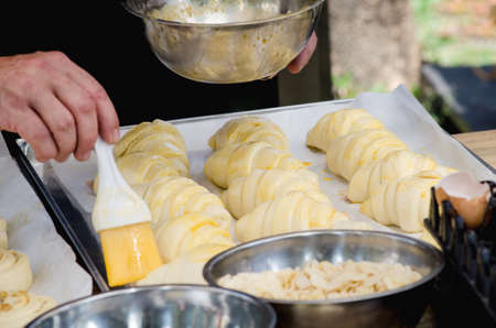 Closed up raw homemade croissant bakery on trey with blur check's hand applying egg to get ready for bakingの写真素材