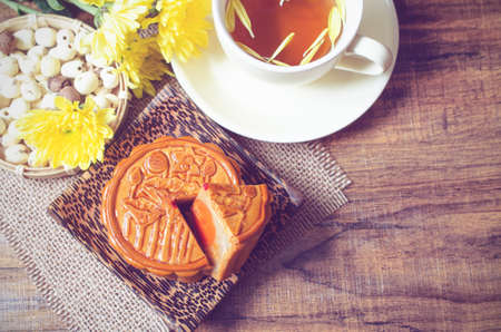 Top view of delicious homemade moon cake on wooden plate with tea cup and chrysanthemum flower in soft light vintage tone. For concept of Chinese Mid Autumn Festival celebrationの写真素材