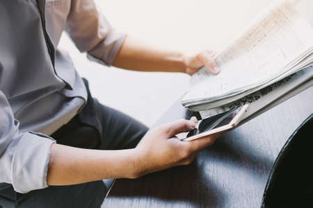 Man's hands holding newspaper and using smartphone for online .の写真素材
