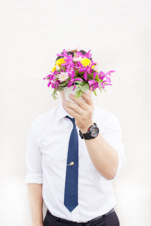 Waiting for his girlfriend. Close up of handsome young man holding bouquet of flowers stand in front of the concrete wall .の写真素材