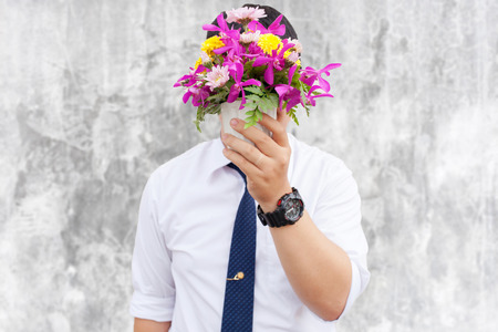 Waiting for his girlfriend. Close up of handsome young man holding bouquet of flowers stand in front of the concrete wall .の写真素材