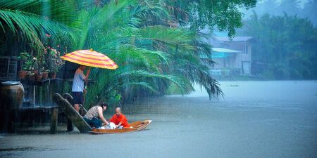 People give food offerings to a Buddhist monk coming by boat, in the morning rain  Amphawa, Thailand のeditorial素材
