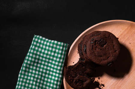 Chocolate cookies are placed in a wooden tray with a green cloth placed over a black background.top viewの写真素材
