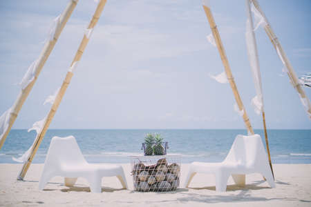 Two white chairs and a table on the sandy beach against the sea backdrop.の写真素材