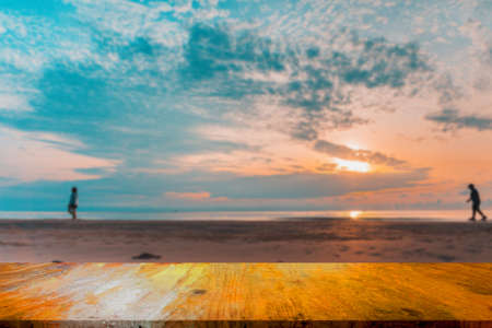 An old wooden table against a sea backdrop with shadows of two walking people.