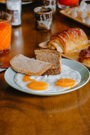 Fried eggs and bread in white plate for breakfast on wooden tableの写真素材
