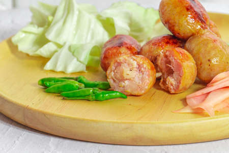 Isaan sausage is one of the famous dishes of Thailand, Isaan sausage is served in a wooden plate on a white table with chili and vegetables to eat together.の写真素材