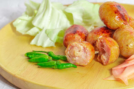 Isaan sausage is one of the famous dishes of Thailand, Isaan sausage is served in a wooden plate on a white table with chili and vegetables to eat together.の写真素材
