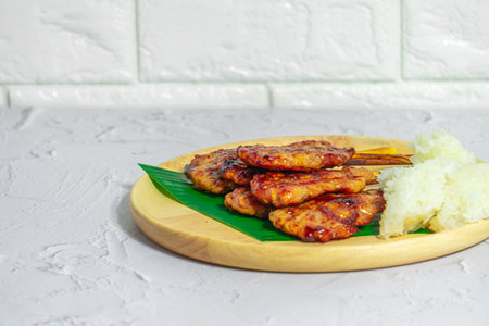 Grilled pork on bamboo skewers placed on a steel grill in a wooden tray with sticky rice in the cart, ready to serveの写真素材