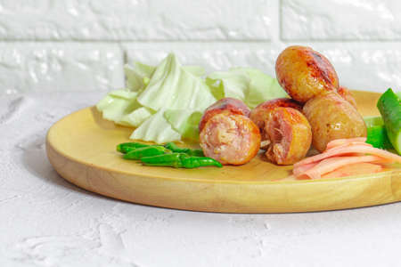 Isaan sausage is one of the famous dishes of Thailand, Isaan sausage is served in a wooden plate on a white table with chili and vegetables to eat together.の写真素材