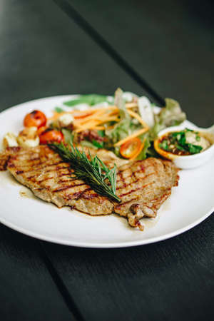 Pork steak with lettuce in white plate on black wooden tableの写真素材