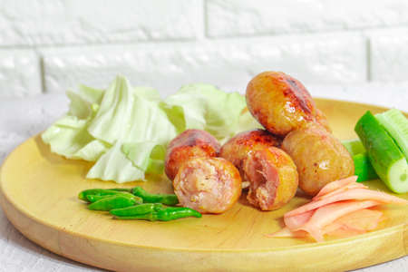 Isaan sausage is one of the famous dishes of Thailand, Isaan sausage is served in a wooden plate on a white table with chili and vegetables to eat together.の写真素材