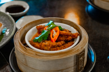 Traditional dim sum chicken feet stewed in dark sauce with chili slices and cilantro garnish served in a bamboo steamer at a Bangkok restaurant.