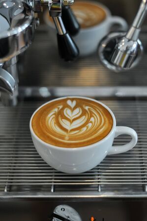 Coffee cup with latte art on the espresso machine trayの写真素材
