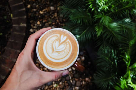 Barista hand holding cup of coffee with his latte art.