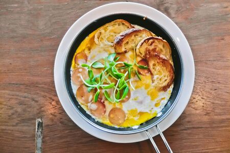 breakfast: fried eggs with croissants and sausage in pan on wood tableの写真素材