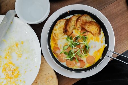breakfast: fried eggs with croissants and sausage in pan on wood tableの写真素材