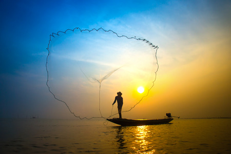 Silhouettes fisherman throwing fishing nets during sunset, Thailand.の写真素材